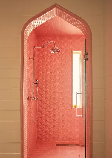 Elegant pink shower with arched entrance, patterned tiles, and a large window bringing in natural light.