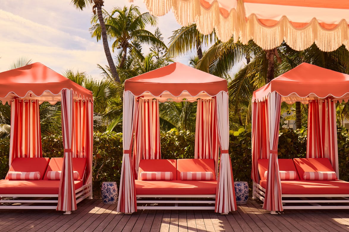Three red cabanas with striped curtains on a sunny patio, surrounded by palm trees.