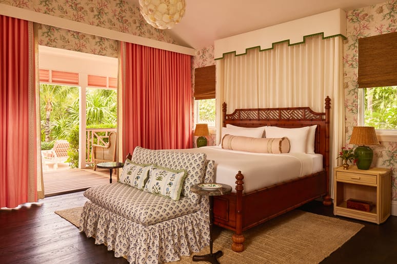 Tropical-themed bedroom with floral wallpaper, elegant bed, and a view of lush greenery through sliding doors.