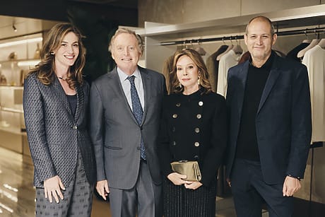Group of four people in formal attire standing in a clothing store with racks of clothing in the background.