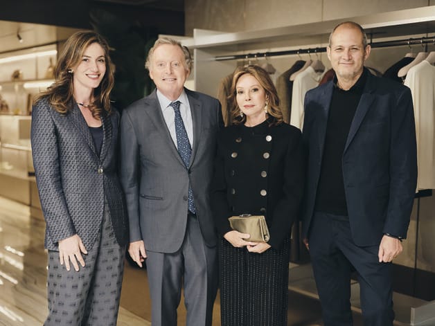 Group of four people in formal attire standing in a clothing store with racks of clothing in the background.