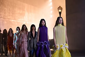 Models in the Dior 2027 cruise Collection walking on runway at LACMA in elegant dresses during a fashion show, dimly lit background with a streetlamp.