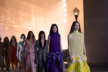 Models in the Dior 2027 cruise Collection walking on runway at LACMA in elegant dresses during a fashion show, dimly lit background with a streetlamp.