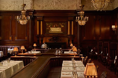 Elegant dining room with ornate chandeliers, wood paneling, and neatly set tables, creating a classic, upscale ambiance.