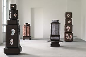 Artistic wooden sculptures with intricate designs displayed in a minimalist gallery setting.