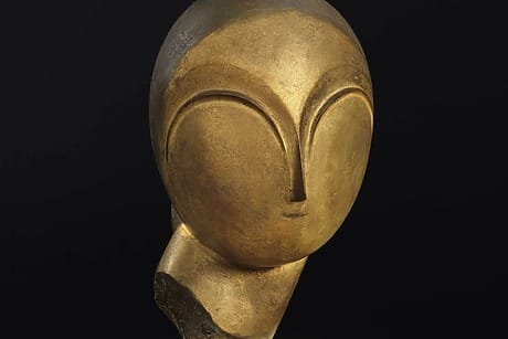 Danaïde by Constantin Brancusi, a gold sculpture of a stylized, abstract human face with smooth features against a dark background, to be auctioned at Christie’s as part of the SI Newhouse sale.