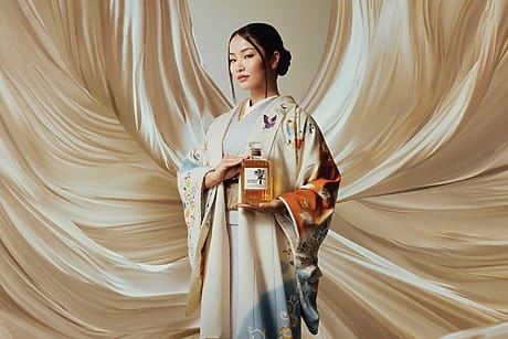 Woman in elegant kimono holds a whiskey bottle against a flowing fabric backdrop.