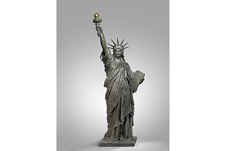Statue of Liberty replica on gray background, torch held high in right hand, tablet in left hand.