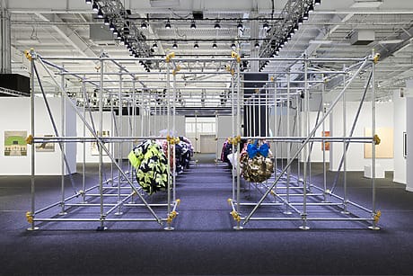 Art installation with geometric metal framework and colorful fabric spheres in a gallery setting with bright overhead lights.