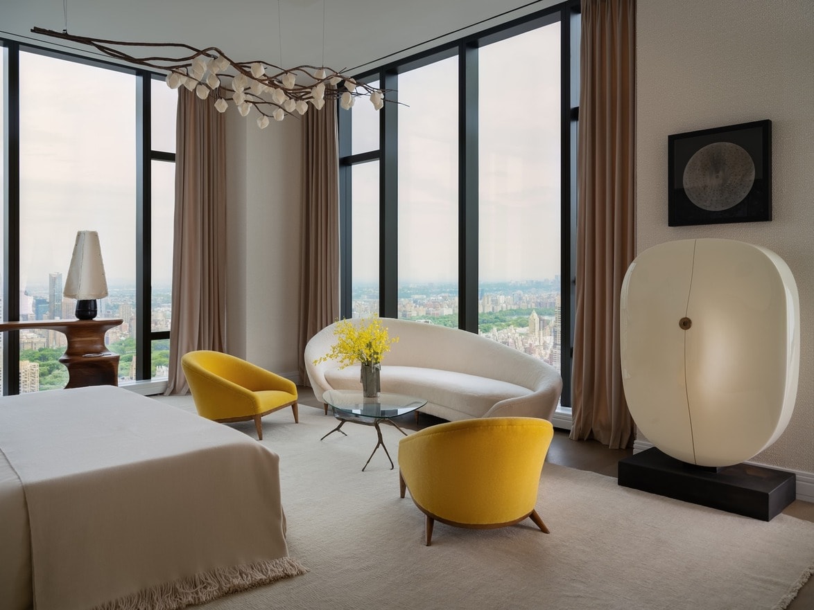 Modern living room with large windows, white sofa, yellow chairs, and contemporary decor.