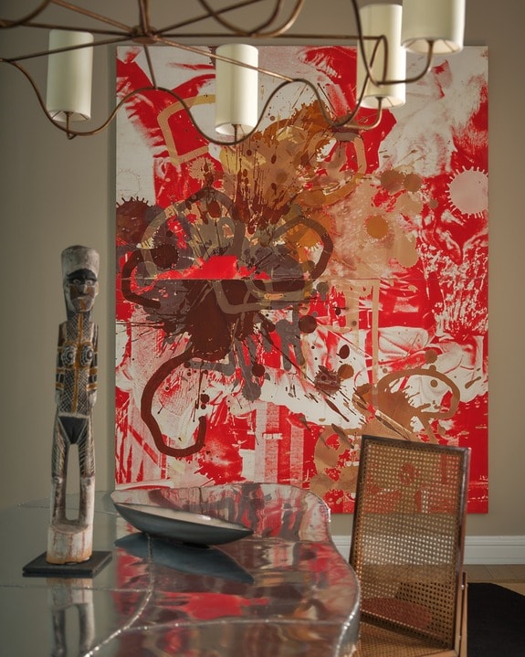 Colorful abstract painting on wall with wood sculpture and metal table in foreground, accented by modern chandelier.