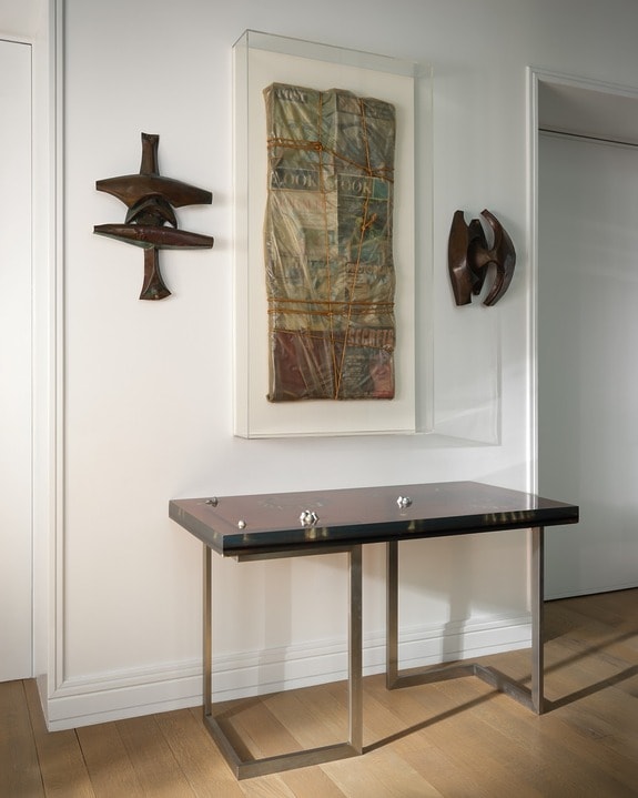 Modern hallway with abstract wall art, sleek black table with metal legs, and wooden floor.