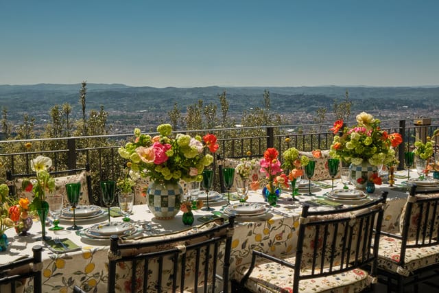 Elegant outdoor dining table with floral arrangements overlooking a scenic vista of hills and a distant town.
