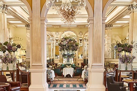 Elegant hotel lobby with ornate columns, chandeliers, and floral arrangements, featuring plush seating and warm lighting.