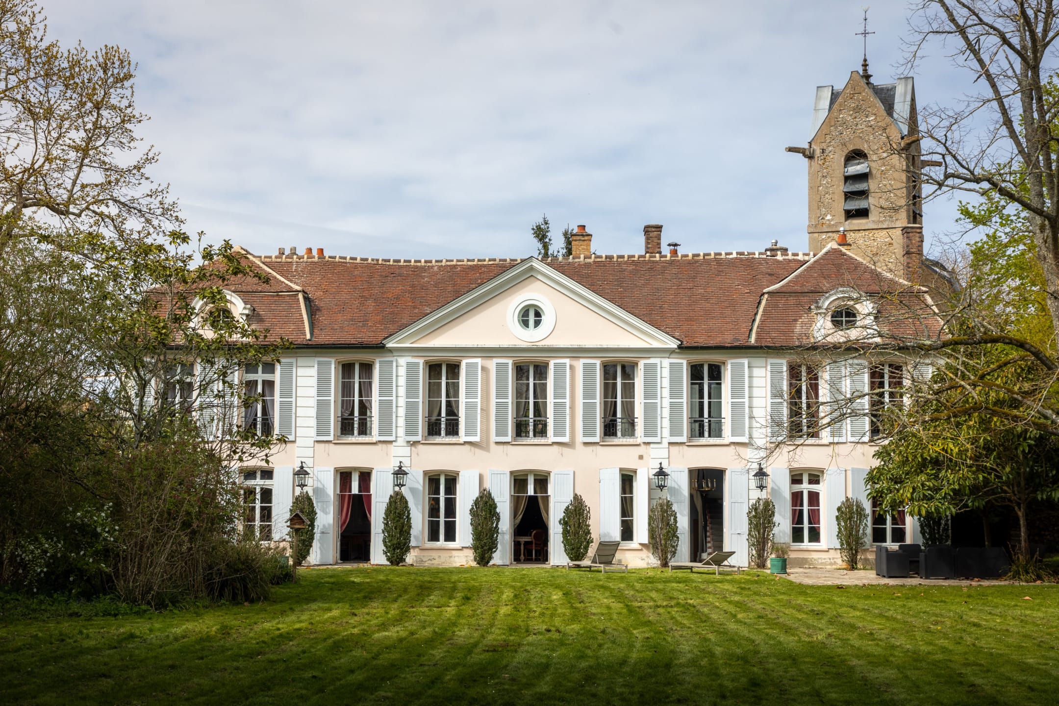 Elegant French chateau with stone facade, tall windows, blue shutters, and a lush green lawn in the foreground.