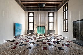Art installation of floating metallic glass pillows in a spacious room with a tiled floor, large windows, and high ceiling.