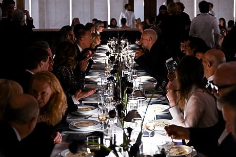People dining at an elegant long table with dim lighting and glasses of wine.