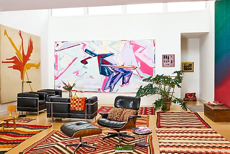Colorful modern living room with abstract paintings, mid-century furniture, and patterned rugs.