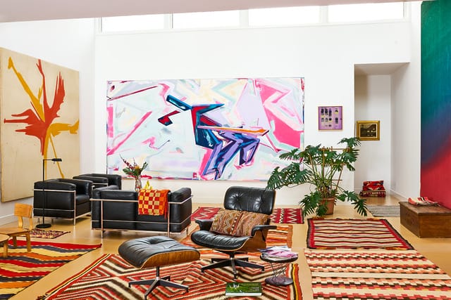Colorful modern living room with abstract paintings, mid-century furniture, and patterned rugs.