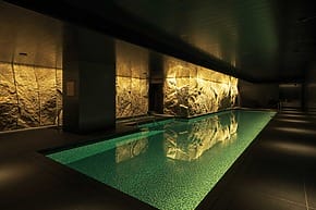Luxurious indoor swimming pool with stone wall, dim lighting, and lounge chairs for relaxation.