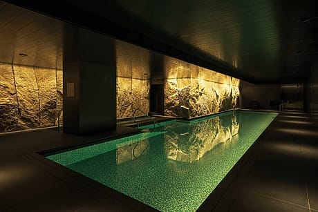 Luxurious indoor swimming pool with stone wall, dim lighting, and lounge chairs for relaxation.