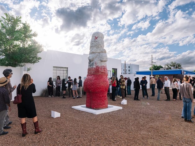 People gathered around a large red and white outdoor sculpture on a sunny day with clouds in the sky.