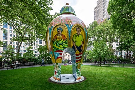 Roberto Lugo's Alfarero del Barrio, a vibrant large vase sculpture in New York's Madison square park with colorful portraits, lush greenery, and surrounding buildings.