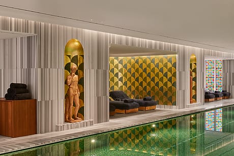 Luxury indoor pool area at the Bulgari Hotel in Rome with stylish seating, geometric patterns, and sculptures, creating a serene and elegant atmosphere.
