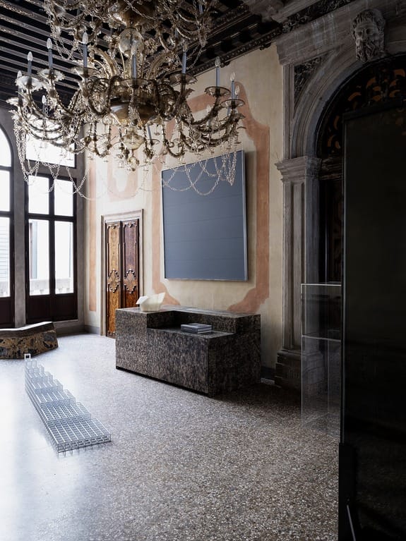 Opulent room with a grand chandelier, modern art, and minimalist furniture in a historic setting.