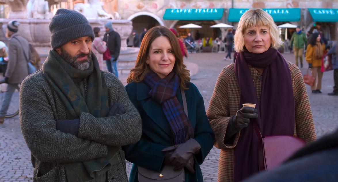 Three people standing outdoors in a casual setting, wearing winter coats and scarves, in front of a cafe background.