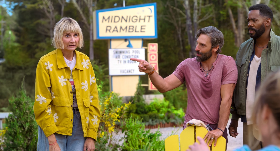 Three people having a discussion outside a motel with a "Midnight Ramble" sign in the background.