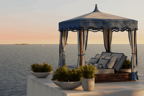 Luxury canopy bed overlooking calm ocean at sunset with soft pink sky.