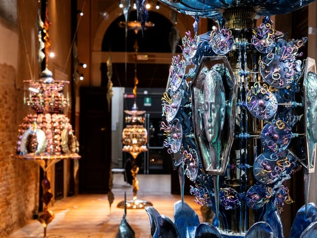 Colorful sculptural art installations displayed in a dimly lit gallery with textured walls and a high ceiling.
