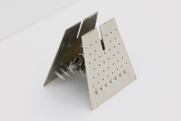 Abstract metal sculpture with perforated sheets and jagged protrusions, positioned on a white background.