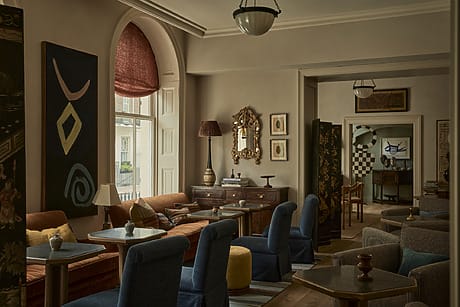Cozy living room with vintage furniture, abstract artwork, and large window with red shade.