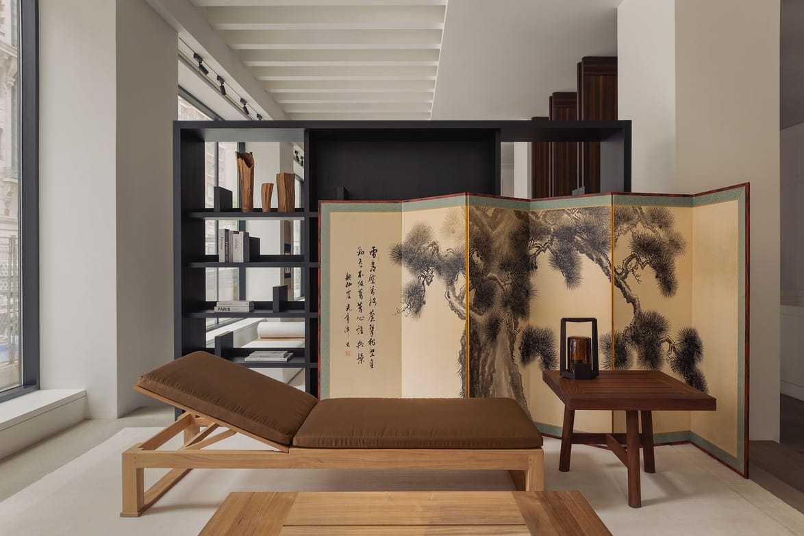 Japanese folding screen with trees and calligraphy near a wooden daybed and table in a modern interior space.