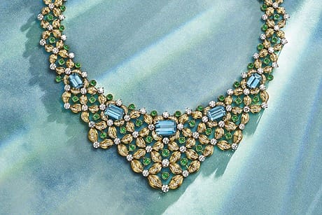 Elegant necklace with blue, green, and gold gemstones on a textured blue-green background.