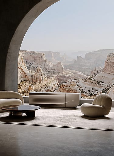 Modern living room with curved sofa and armchair overlooking a scenic rocky canyon through large arched window.