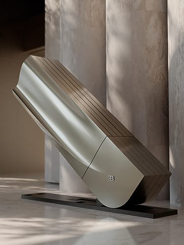 Sleek metallic sculpture in a minimalist indoor setting with soft lighting and marble accents.