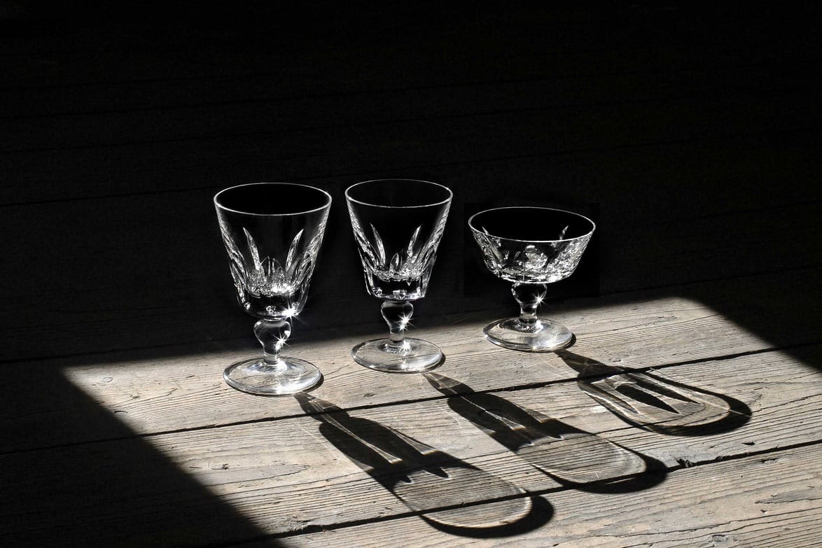Three decorative goblets casting shadows on a wooden floor illuminated by sunlight.