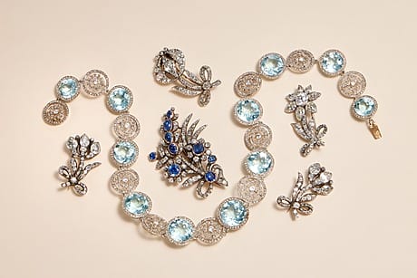 Jewelry from the former Russian Crown Jewels set with blue and clear gemstones arranged on a beige background.