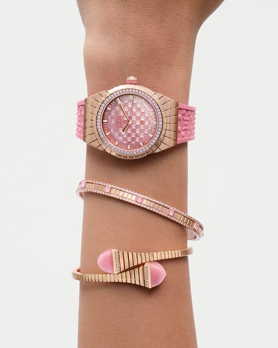 Pink and gold wristwatch with matching bracelets on a person's arm against a plain background.